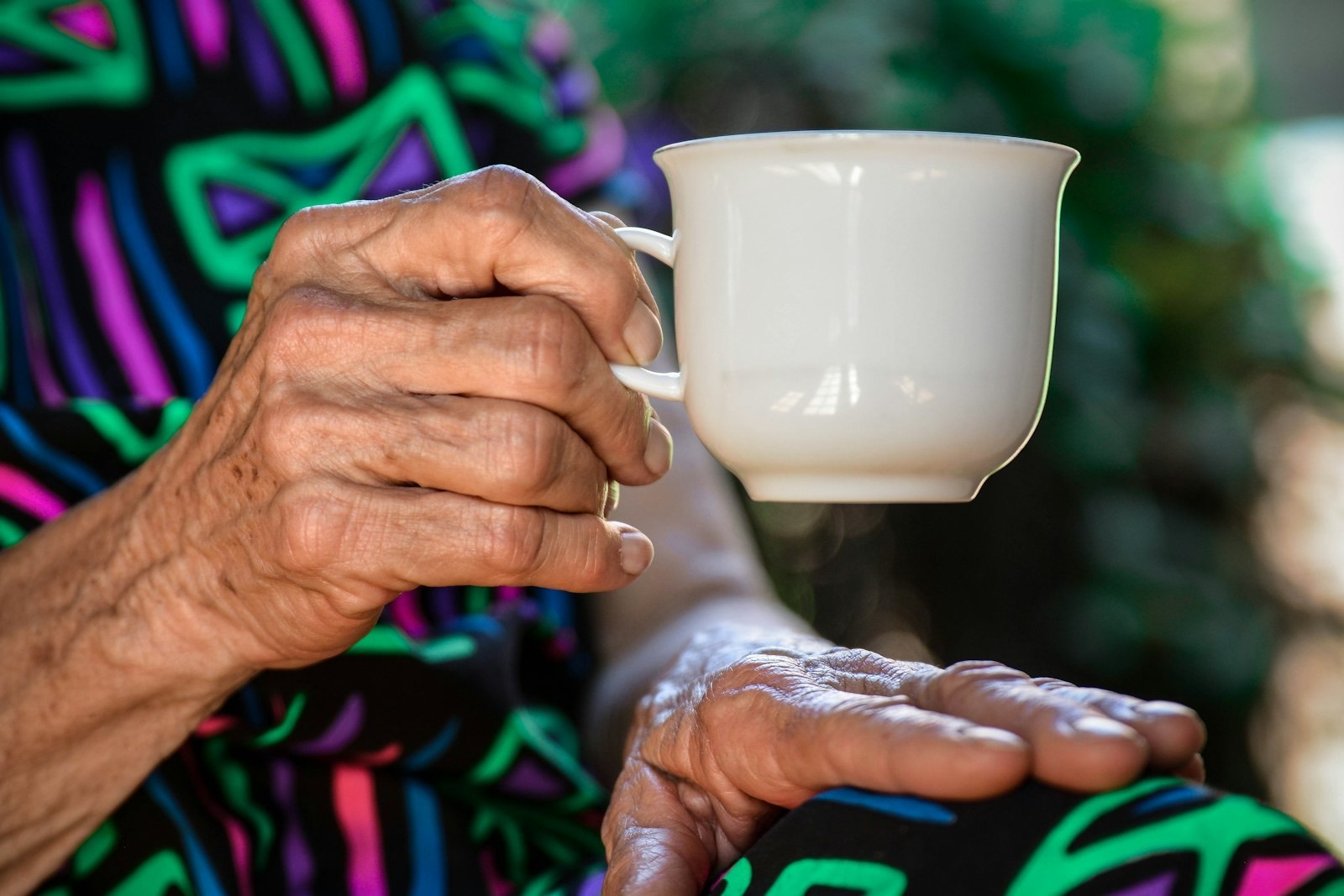 An older woman’s hands holding a white teacup.